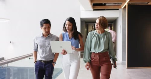 Walking in office, business colleagues discussing work while using laptop
