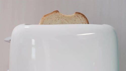 Piece of bread pops out of white toaster on a white background, front view.