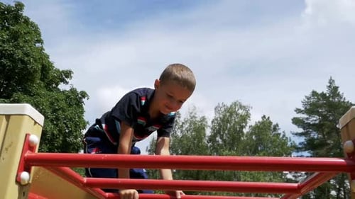 Young Boy Hang the Bar By His Hand to Exercise at Outdoor Playground Against the Sky in Slow Motion