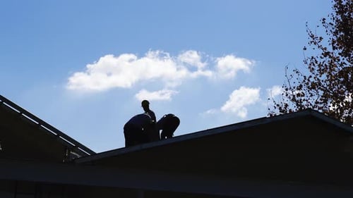 Silhouette of builders working on roof of house, blue sky