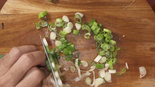 Chef cutting the stalks of fresh spring onions with a sharp knife on a wooden chopping board