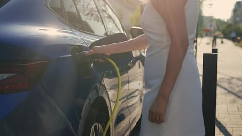 Woman Charging Electric Car on City Street