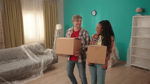 Young Couple with Cardboard Boxes in Their Hands in a New Apartment European Guy and an African