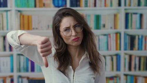 A Woman in Glasses Critiques Her Library Surroundings with a Thumbs Down