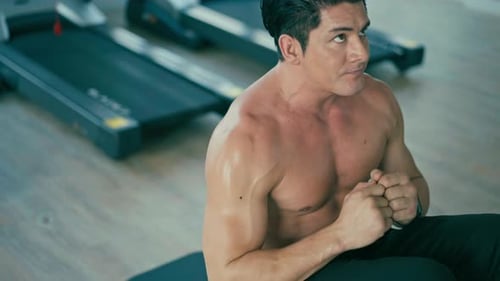 A shirtless muscular man doing sit-ups in a gym