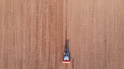 Tractor working agricultural field, cultivating and ploughing dry soil, aerial view.