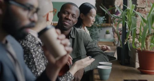 Multiethnic Group of Businesspeople Sitting in Cafe Talking Drinking Coffee and Using Laptop