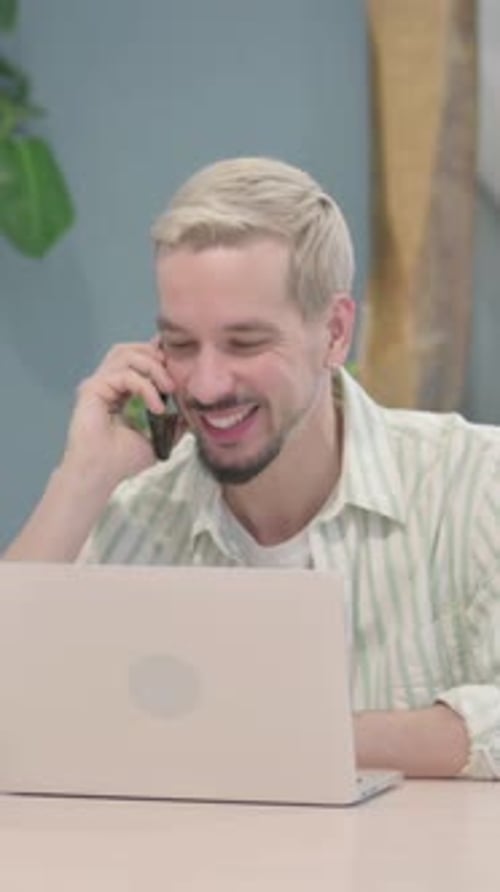 Smiling Man Talking on Phone While Using Laptop