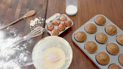 Freshly baked cupcakes, mixing bowl, utensils and used ingredients on kitchen worktop, slow motion