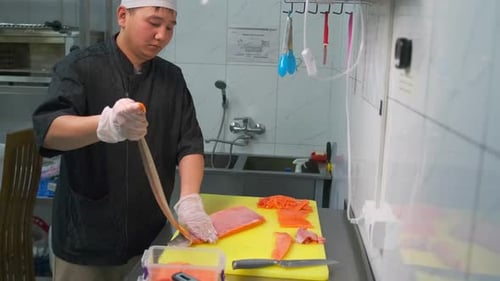 a sushi restaurant chef removes the skin from fresh sea salmon while prepare red fish fillet