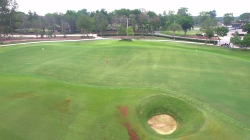 Aerial drone view flying over empty golf course surrounded by lush greenery.