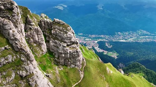 Grey cliffs covered with green grass. Spectacular scenery of the village at the mountain foot.