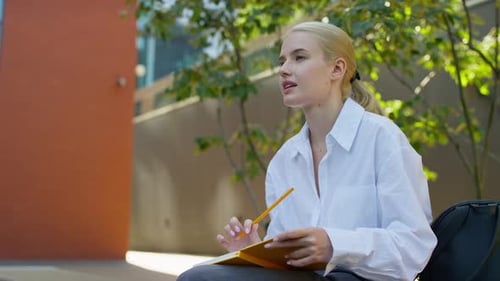 Young Woman Writes in Notebook on City Bench