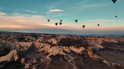 Cinematic drone view low over Cappadocia rocks with numerous floating hot air balloons