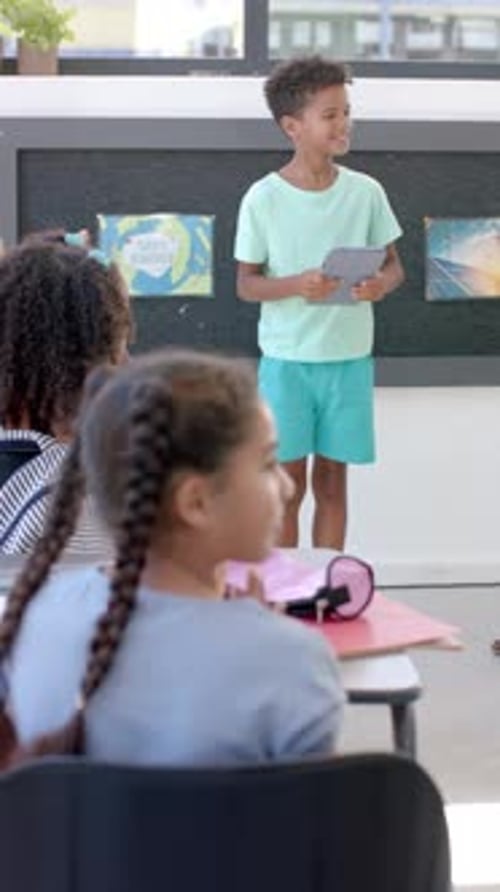 Vertical video: In school, boy holding a tablet stands presenting