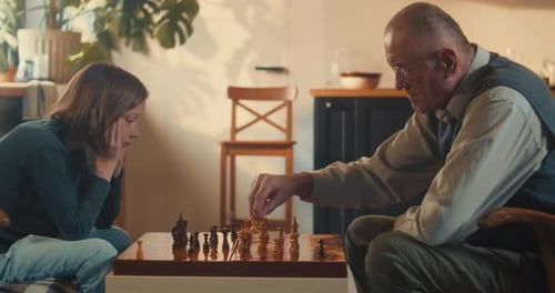 Seitenansicht Cleveres junges Mädchen konzentriert sich auf das Schachspielen mit dem älteren Großvater im Wohnzimmer