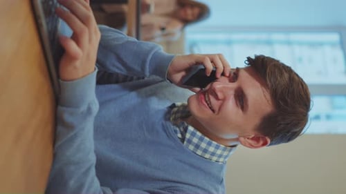 Vertical Screen: Businessman working on laptop and talking on phone in cafe