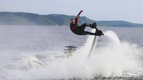 Flyboarding is a New Extreme Sport Where a Joyful Male Flyboarder Flies Over the Water and Performs