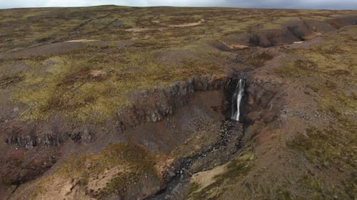 Aerial footage closing up on a majestic waterfall located in the mountains of Iceland.
