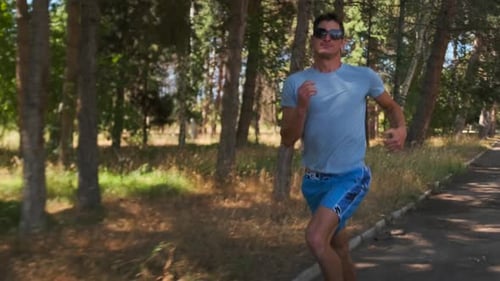 Fit man in sunglasses running fast athlete training endurance on country park at sunny morning