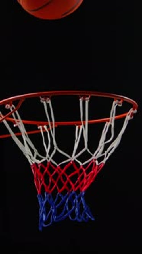 Basketball Falling Through Hoop Net on Black Background