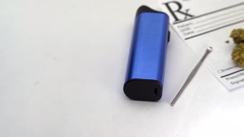 Close up pans across a vaporizer and metal scoop lying on a prescription note. Orange pill bottle li