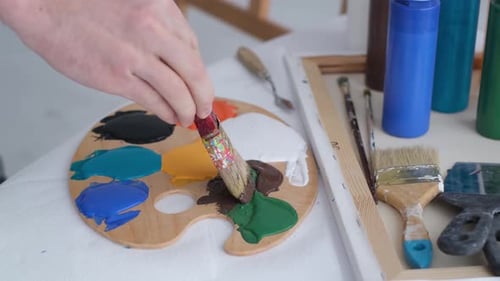 The Hand of a Young Artist Mixes Paints on a Palette That Stands on the Table