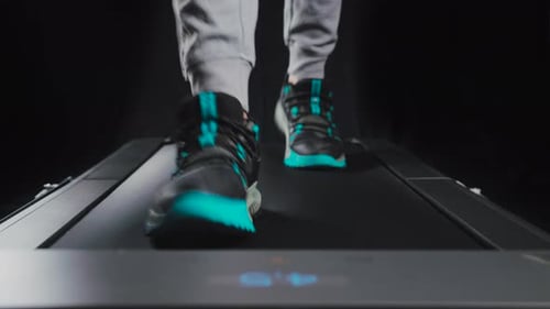 Static frontal close up shot of a man's feet walking on a treadmill