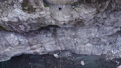 Luftaufnahme eines Mannes, der mit festem Kabel und Schiebeplattform eine steile Flussschlucht überquert