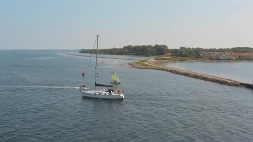 Filmmusik Drohne//Luftaufnahme eines auf dem Meer segelnden Bootes mit einem Yachthafen im Hintergrund mit Meer