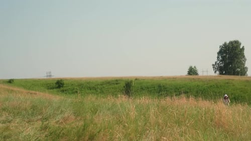 Woman Walking Through Distant Green Field Under Clear Summer Sky