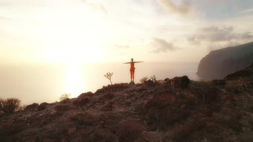 Person standing with arms outstretched overlooking the ocean during sunset at Los Gigantes Cliffs in