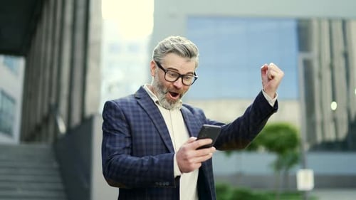 Excited Man Reacting to Smartphone News in City
