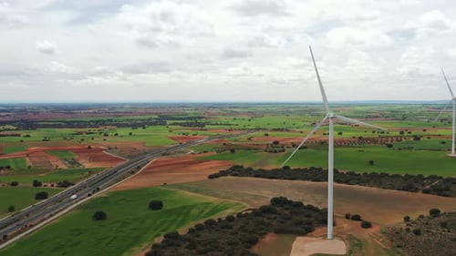 Spinning Wind Turbines Spread Across Farmland Along Highway