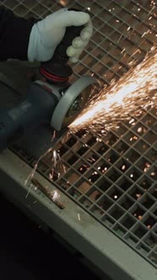 Travailleur utilisant une meuleuse d'angle pour couper du métal dans un environnement industriel, créant des étincelles lumineuses à la verticale