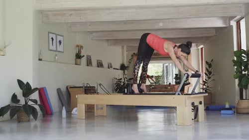 Fit senior caucasian woman stretching on reformer in pilates studio, unaltered, in slow motion