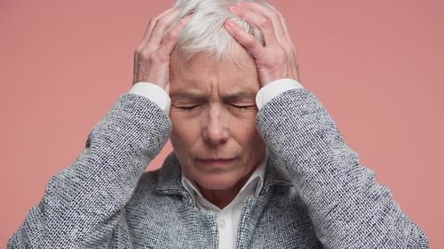 Senior Woman Suffering From Severe Headache on Pink