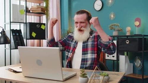 Senior Man Cheering While Using Laptop in Home Office