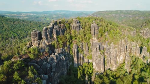 A jagged rocky cliff formation with scattered trees stands prominently over the lush green landscape