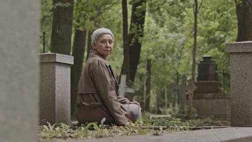 Erwachsene Frau sitzt auf einem Grabstein auf dem Friedhof