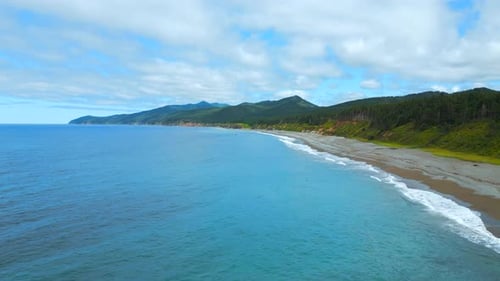 Top view of coastline of coast with mountains on horizon. Clip. Island with green forest