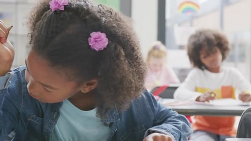 Video of portrait of happy biracial schoolgirl sitting at desk working in school class
