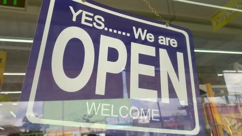 An open sign hanging on the front door of the supermarket
