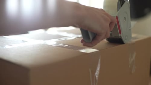 Person Sealing Cardboard Box with Tape Dispenser