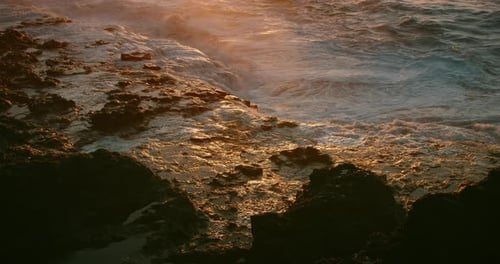 White Foamy Ocean Waves Breaking on Rocky Beach at Golden Sunset Light Closeup Slowmotion Raging