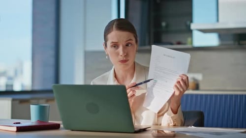 Online Tutor Showing Papes to Laptop Webcam Sitting Modern Kitchen Closeup