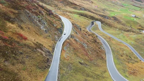 A car on Furka pass road in Switzerland in autumn . Aerial view . wet winding road, rainy day.