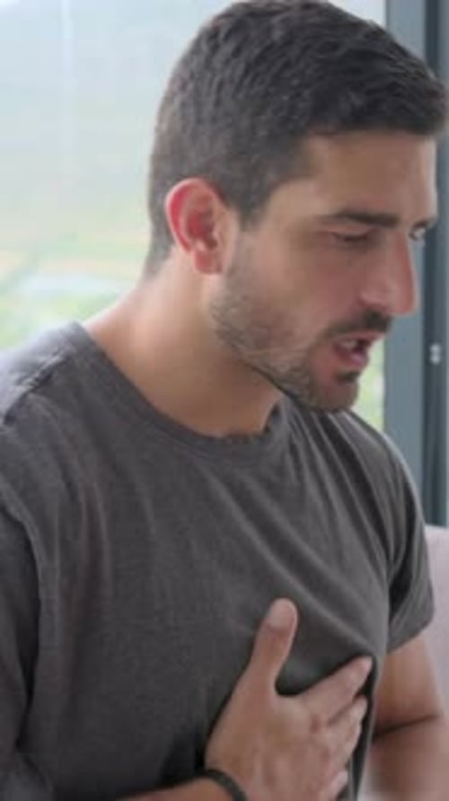 Vertical video: Breathing, man in dark tee checking small green inhaler near window, copy space