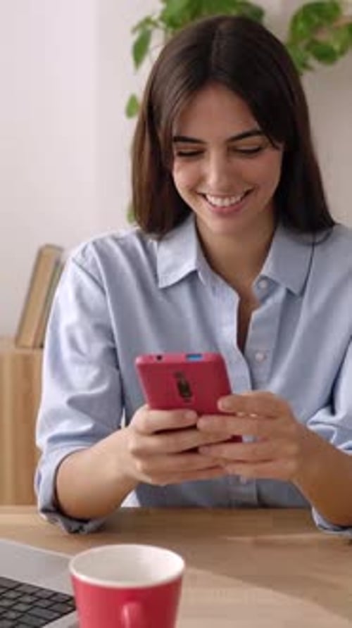 Young Adult Business Woman Using Mobile Phone While Working on Laptop at Home