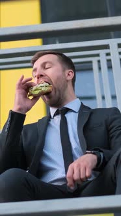 Young Adult Man Eats Sandwich on Stairs